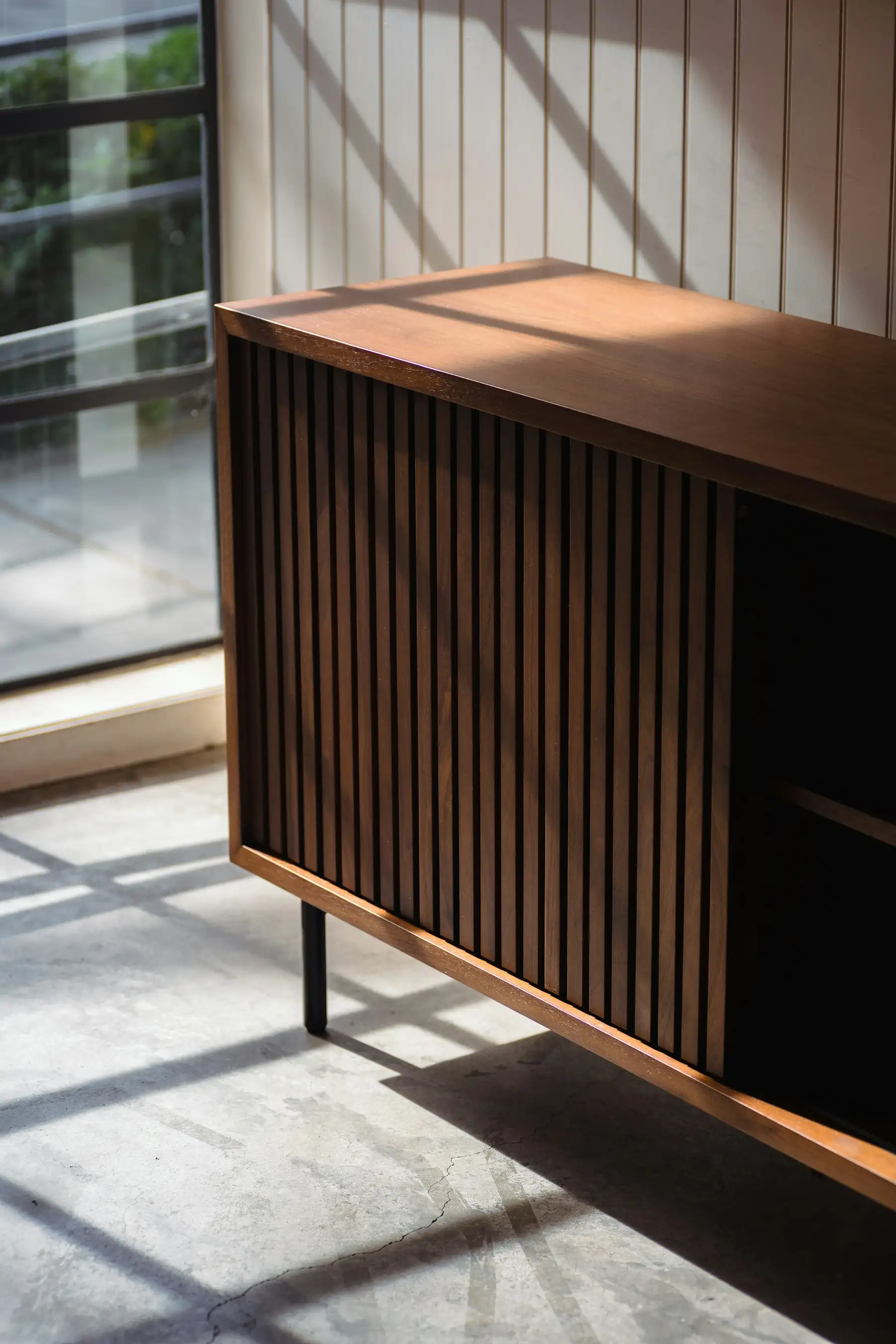 Niedriges Sideboard aus Nussbaum mit vertikal gelatteter Front im Licht eines Fensters