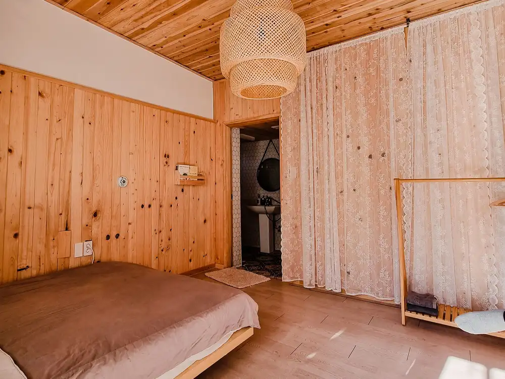Ganz mit hellem, astigem Holz verkleidetes Zimmer mit sichtbarem Balken und Rattanleuchte