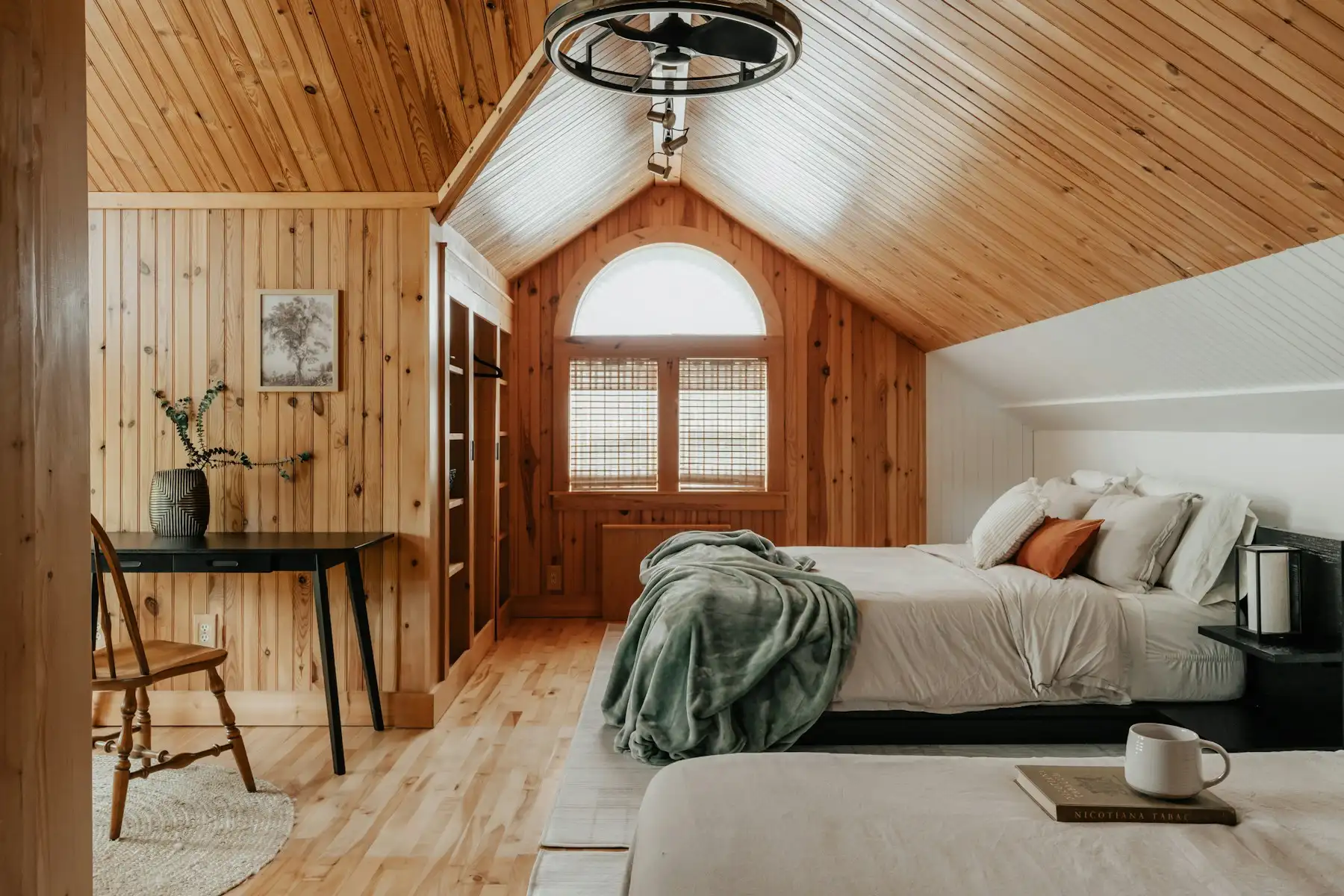 Chambre mansardée lambrissée en pin noueux, fenêtre cintrée et bureau en bois