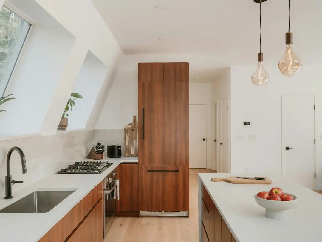 Cuisine sous les combles avec fenêtres de toit, colonne et façades en noyer, plan de travail clair