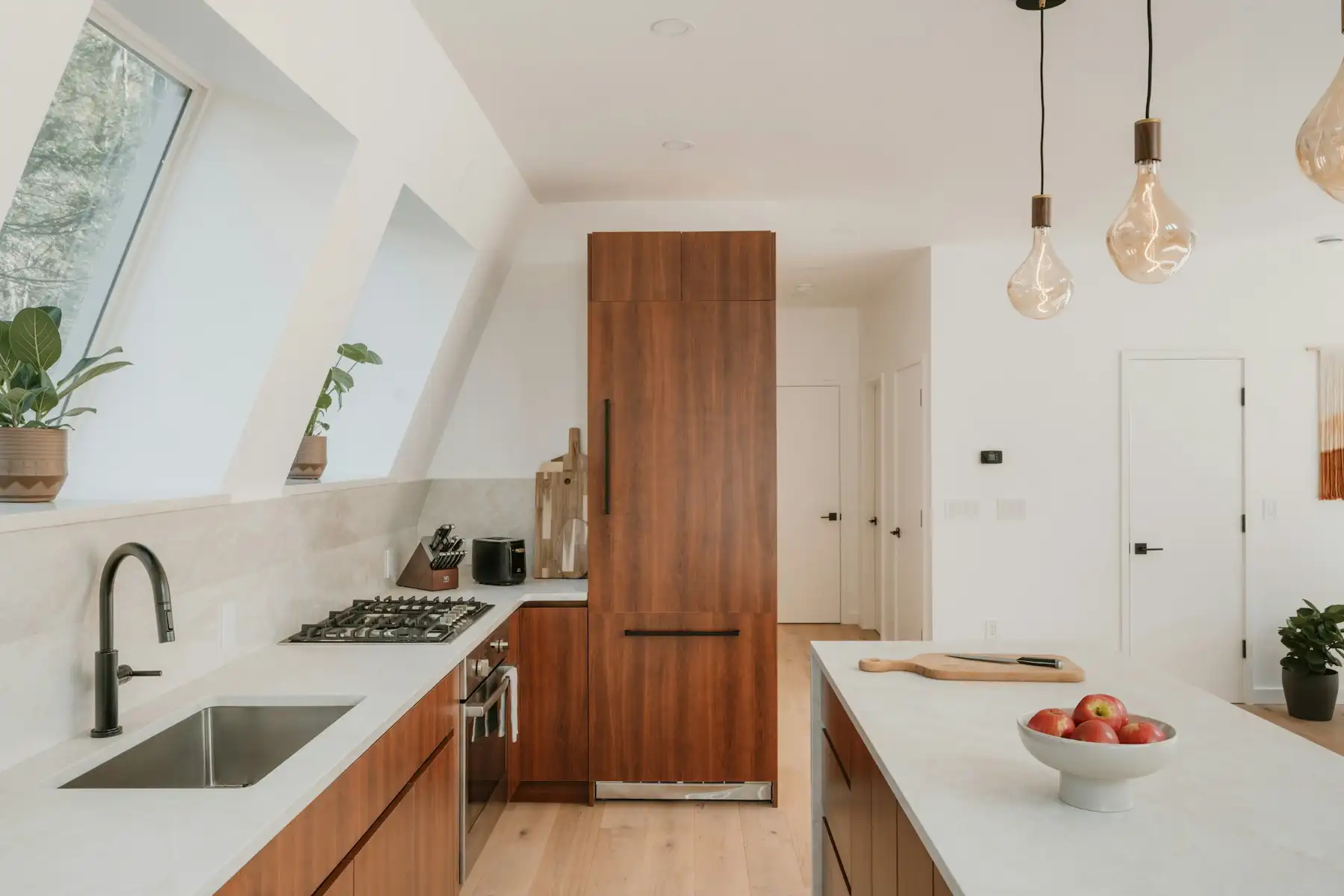 Cuisine sous les combles avec fenêtres de toit, colonne et façades en noyer, plan de travail clair