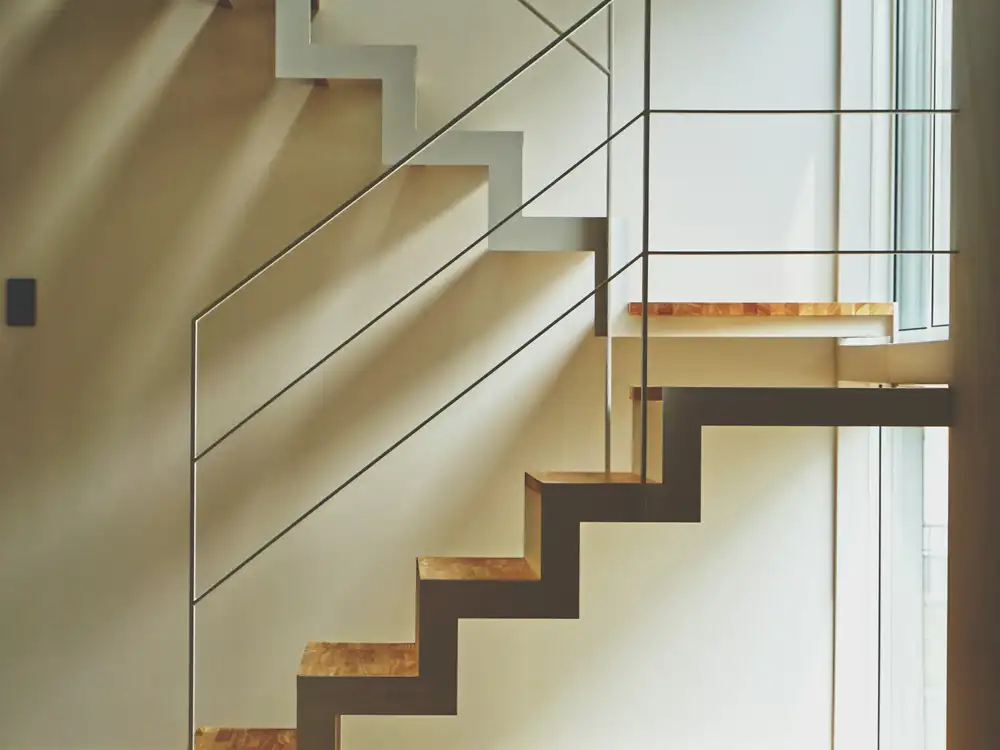 Escalier aux marches en bois et limon métallique blanc, baigné de soleil sur un parquet