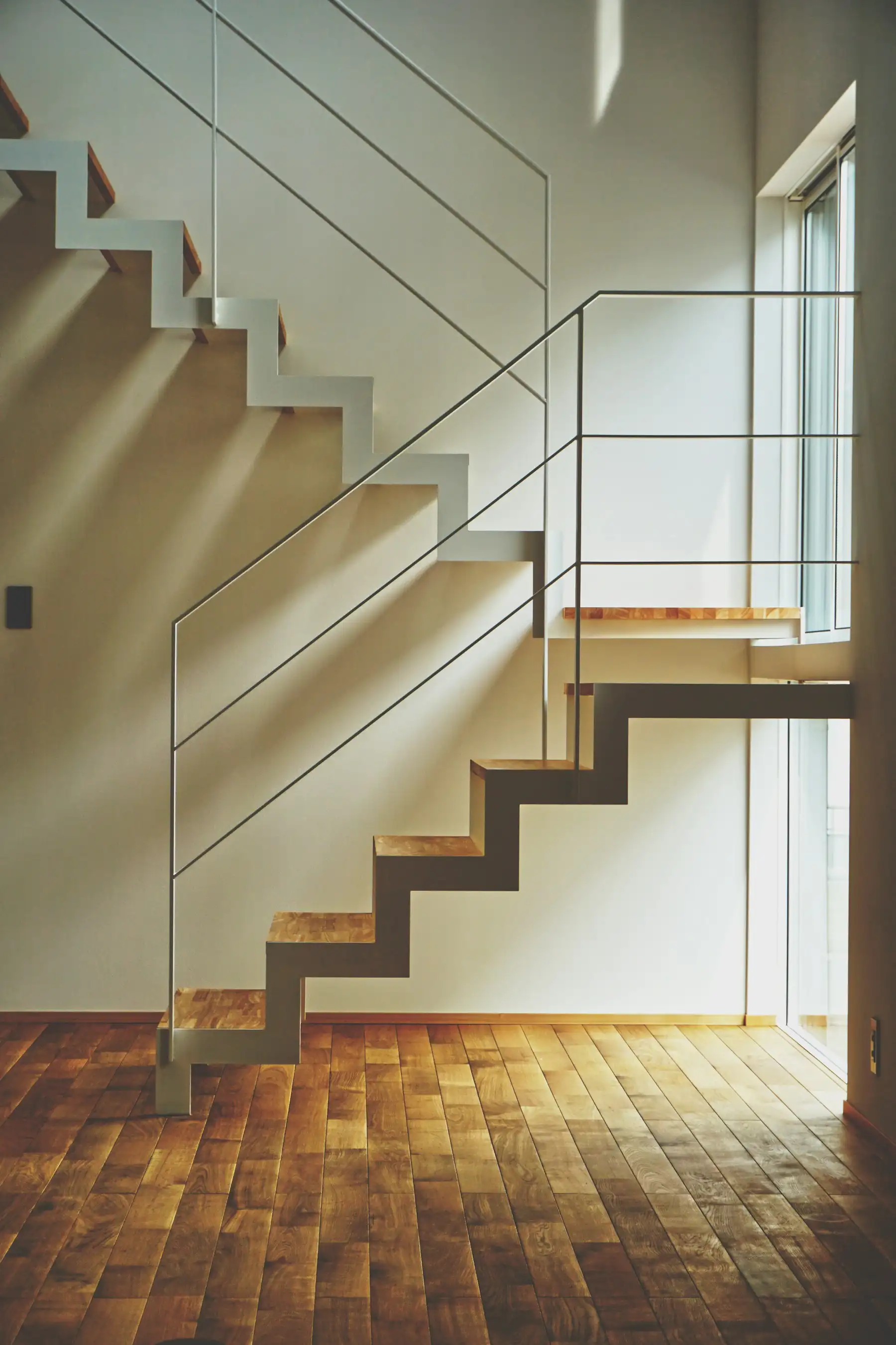 Escalier aux marches en bois et limon métallique blanc, baigné de soleil sur un parquet