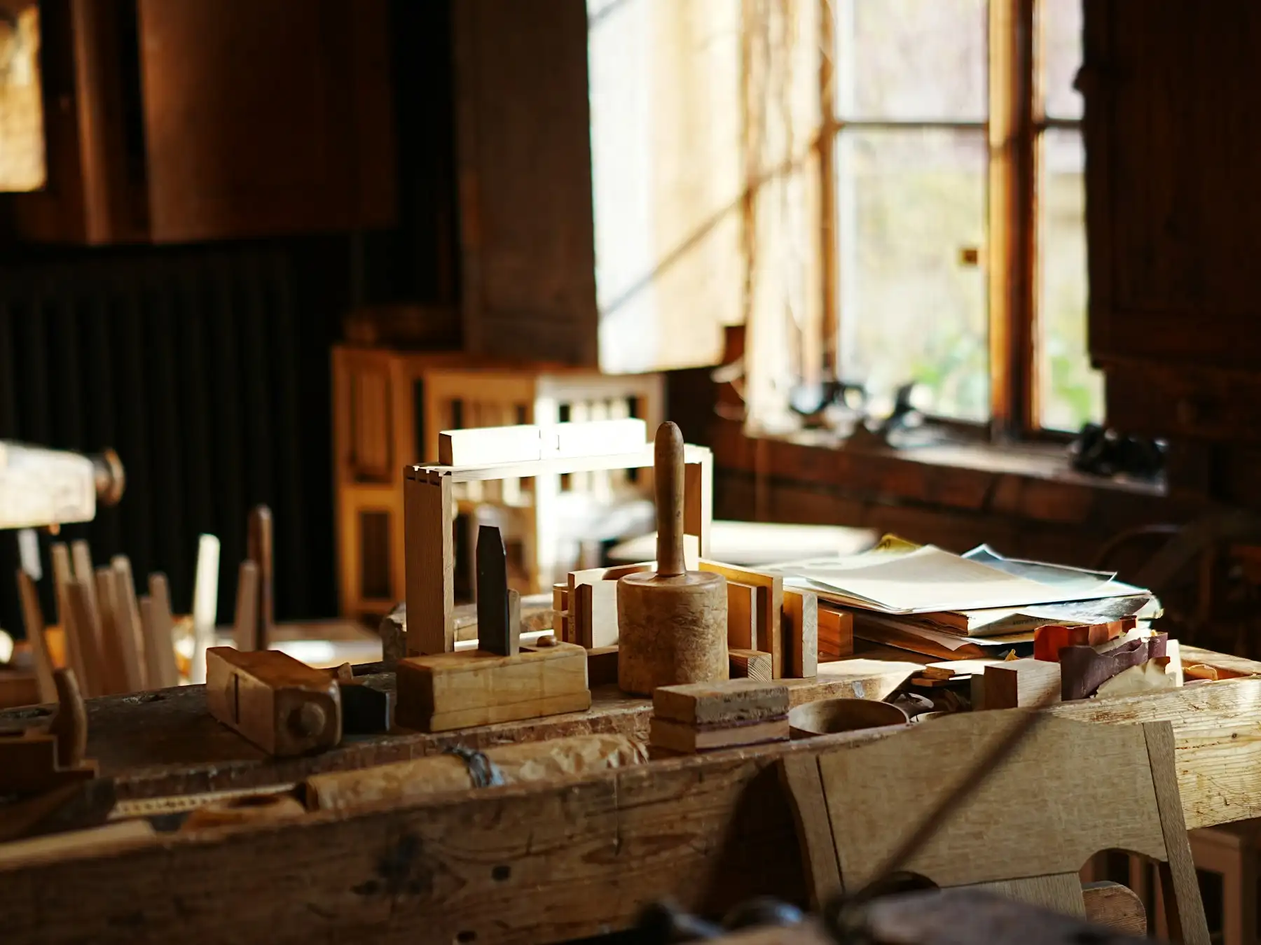 Vieil établi encombré d’outils à main et de pièces de bois dans la lumière rasante d’une fenêtre d’atelier