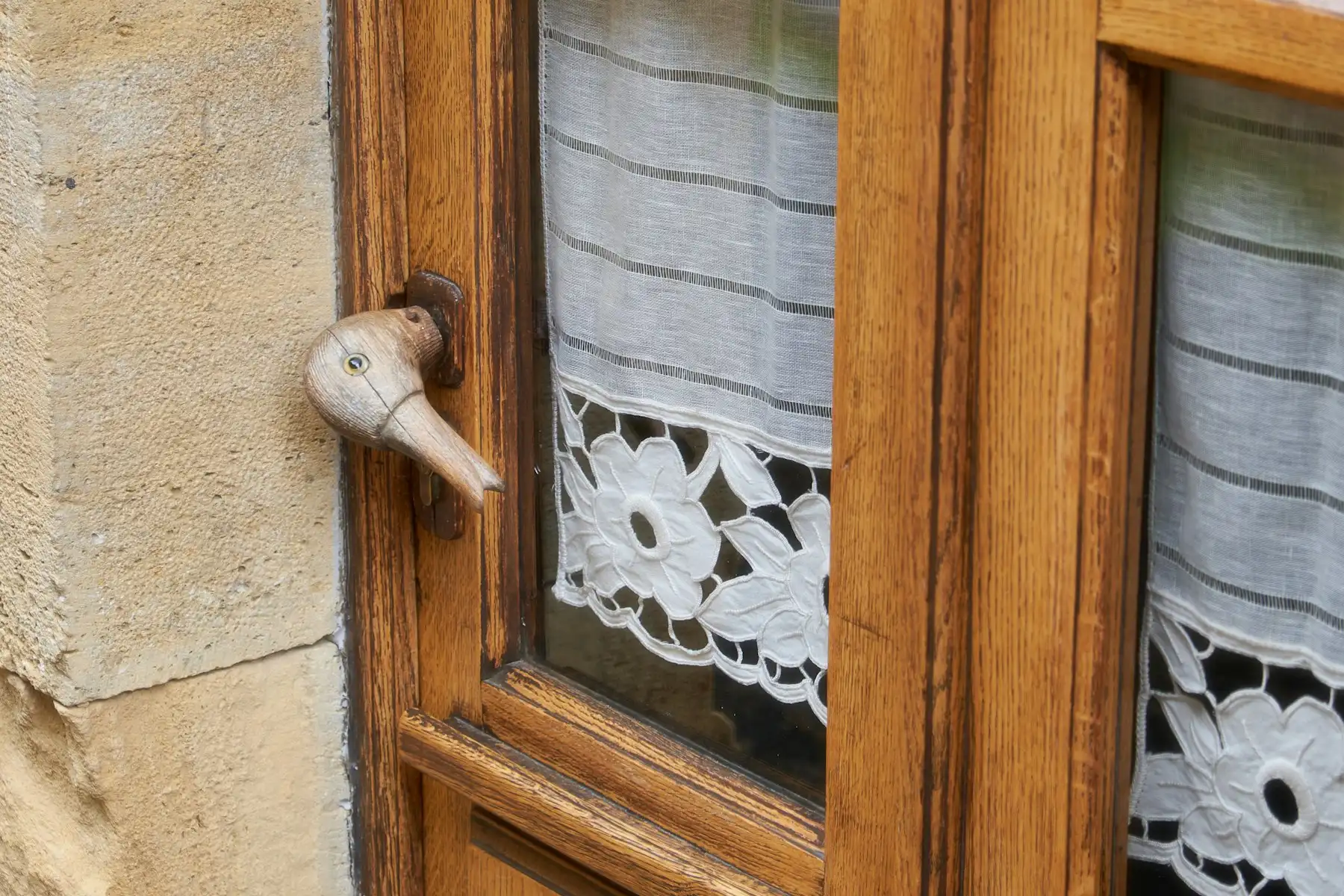 Detail eines lackierten Holzfensters mit Fenstergriff und besticktem Vorhang