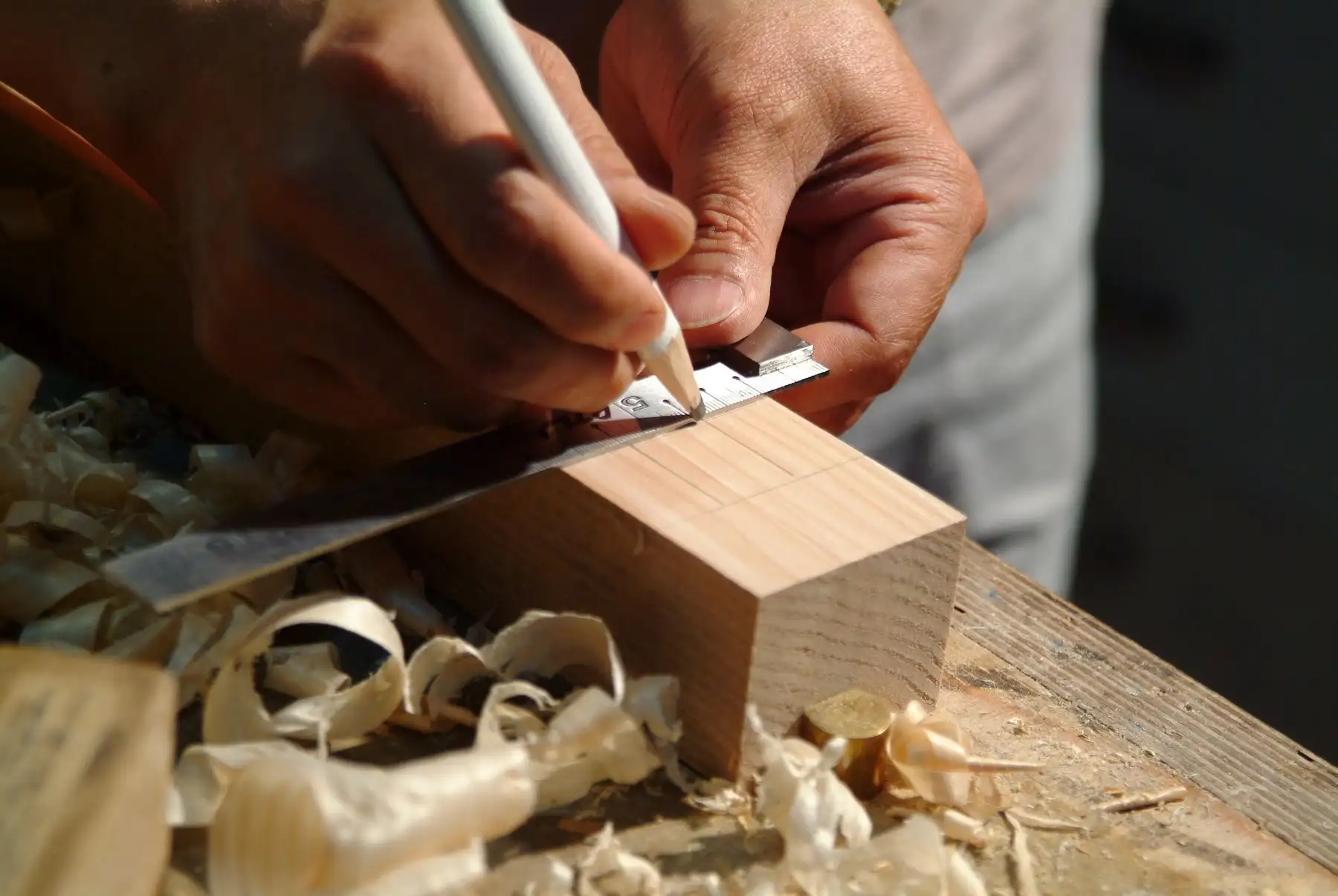 Anreissen mit dem Winkel an der Kante eines Holzstücks, Hobelspäne auf der Werkbank